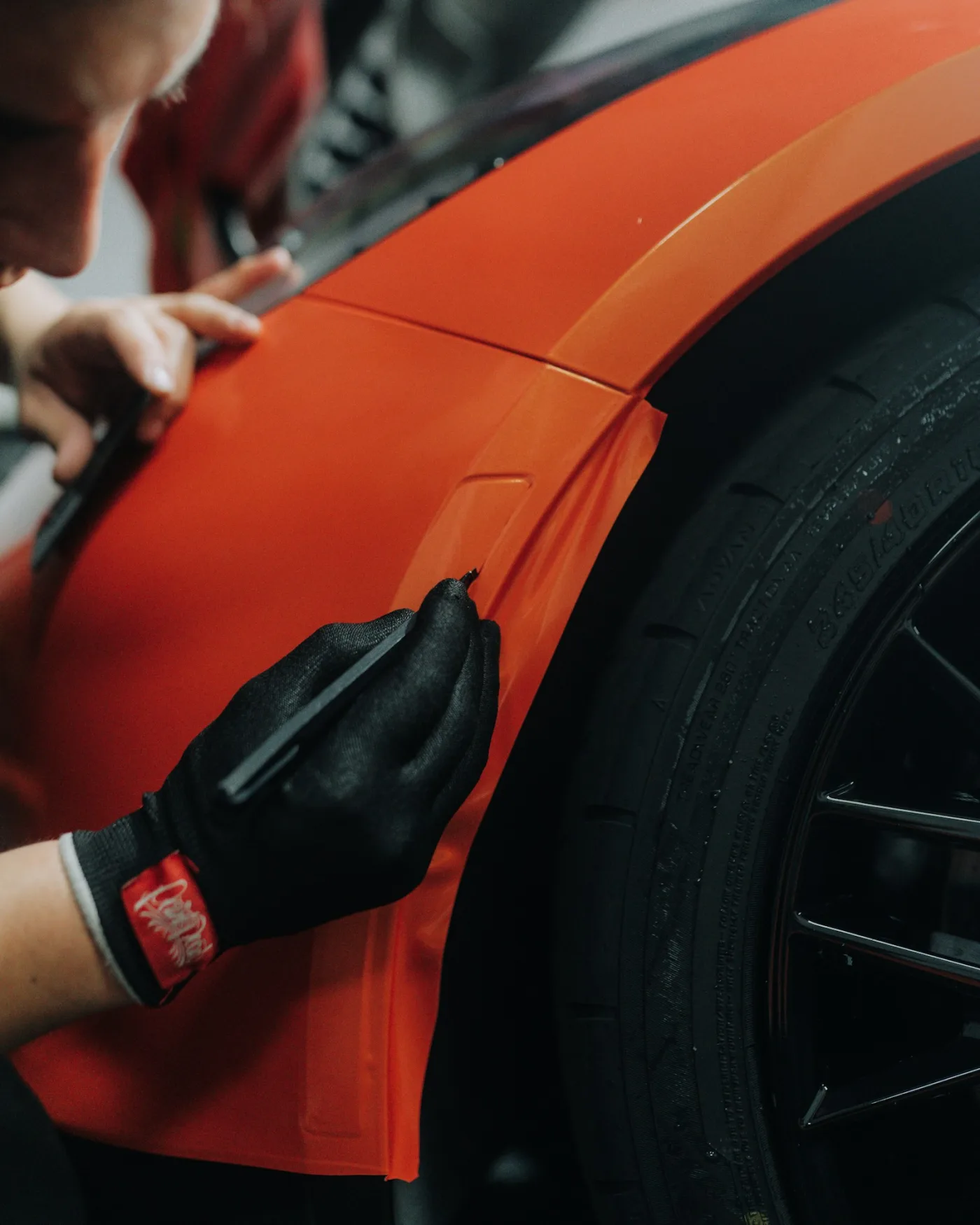 Installer trimming orange vehicle wrap film around a car wheel arch