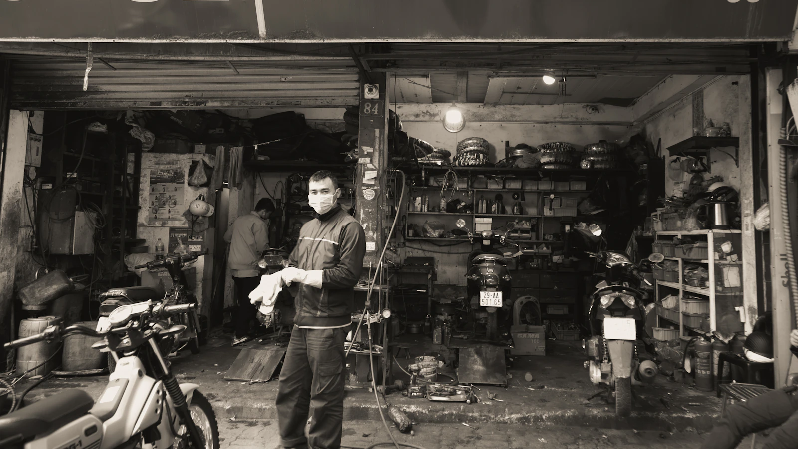 A person standing among motorcycles and tools in a small repair workshop.