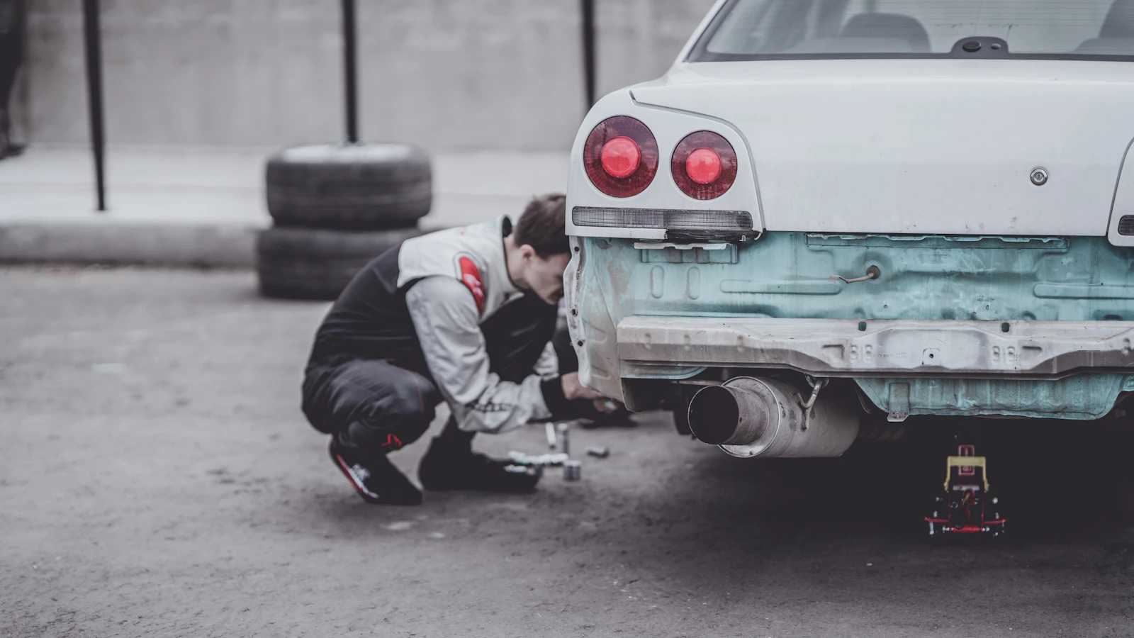 A person working at the rear of a car with its rear bumper removed.
