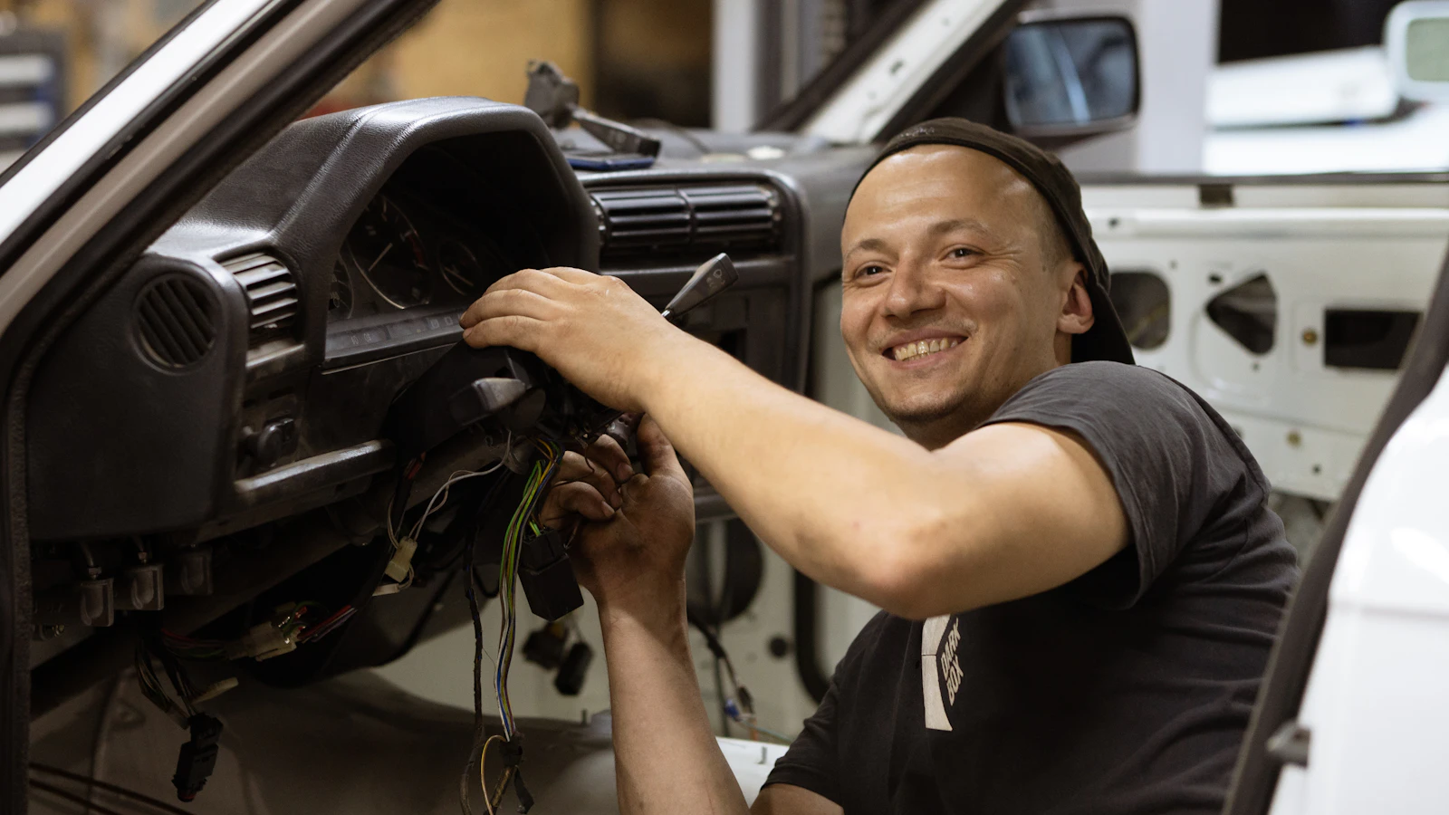 A mechanic working inside a vehicle near its steering wheel and dashboard.