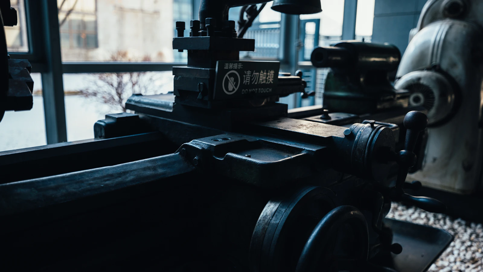 The carriage and handwheels of a metal lathe inside a workshop.