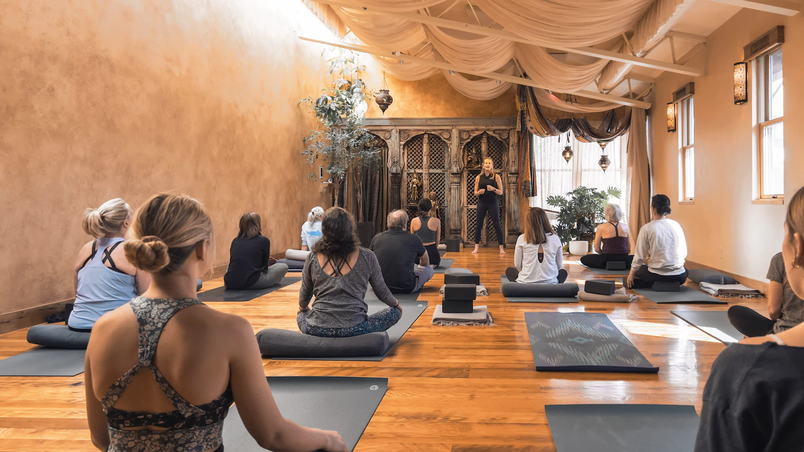 People seated on mats during a class in a yoga studio.