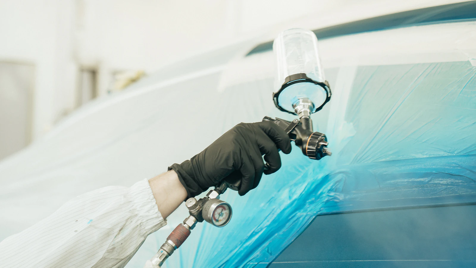 A person wearing protective clothing spraying a masked vehicle panel.