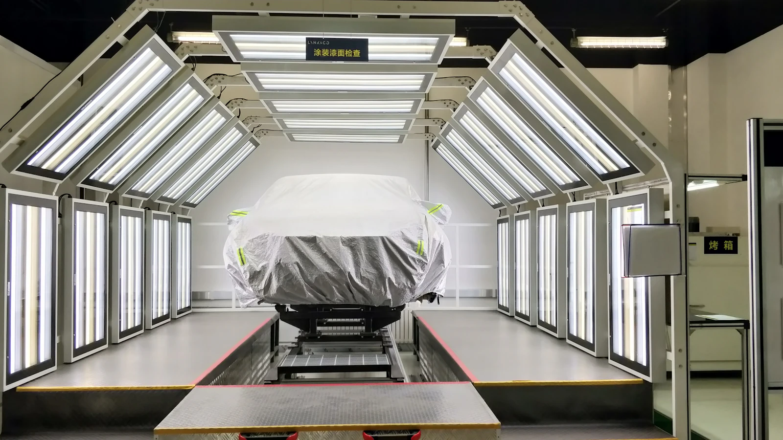 A masked vehicle inside a brightly lit automotive paint booth.