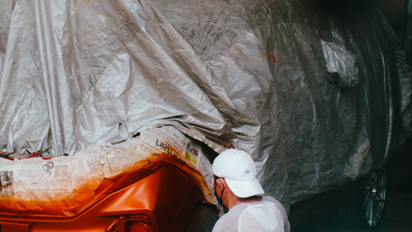 A person working beside an orange vehicle partially covered with masking material.