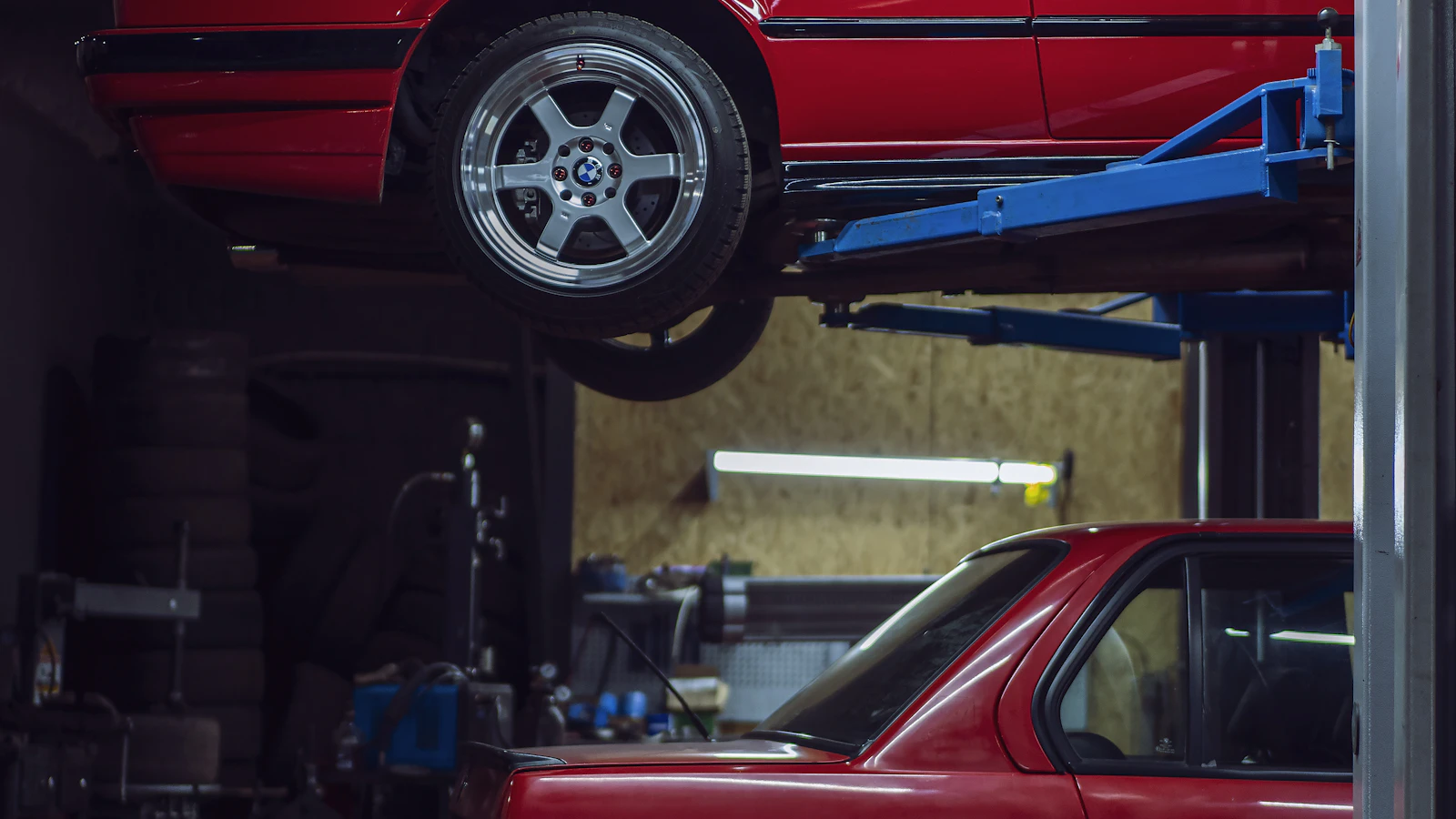 Two red vehicles inside a workshop, with one raised on a lift.