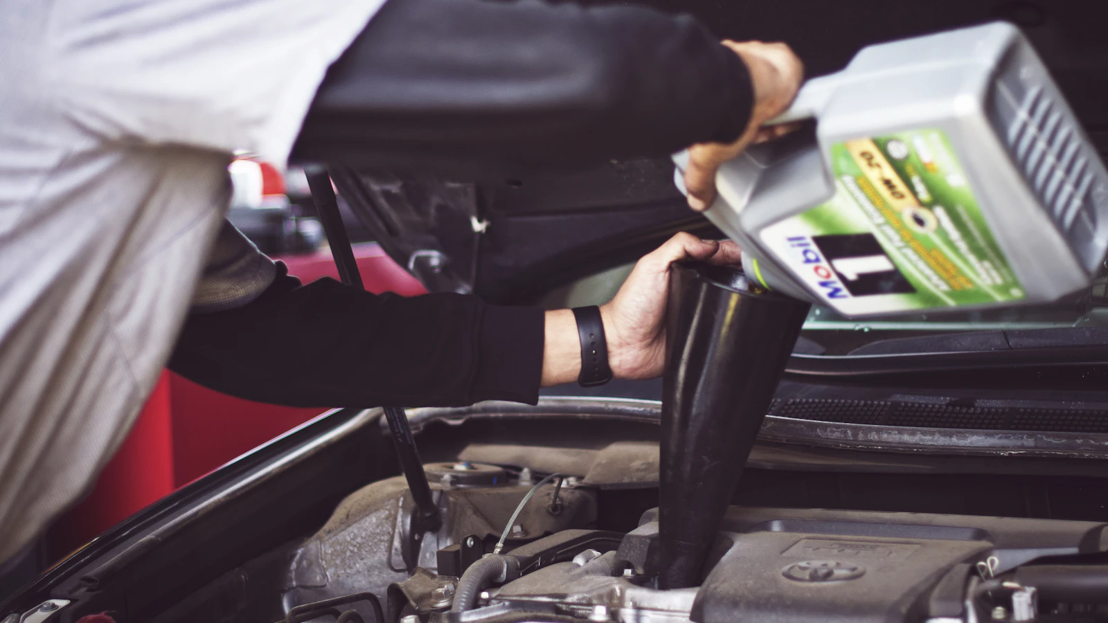 A person pouring oil from a container into a vehicle engine.