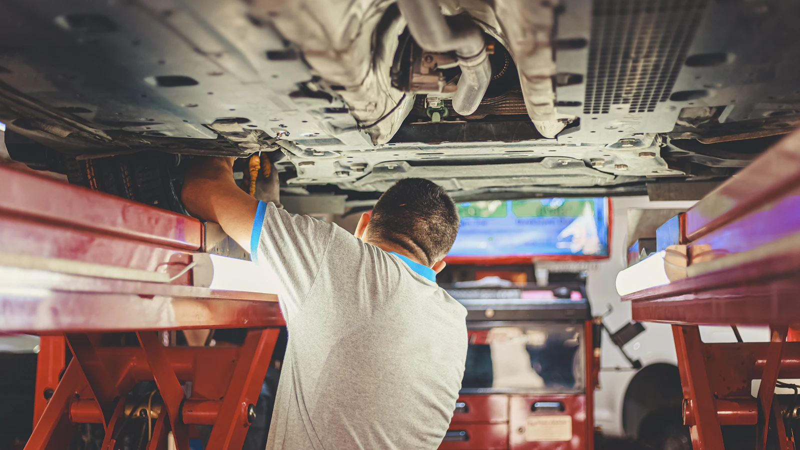 A person working beneath a vehicle raised on a workshop lift.
