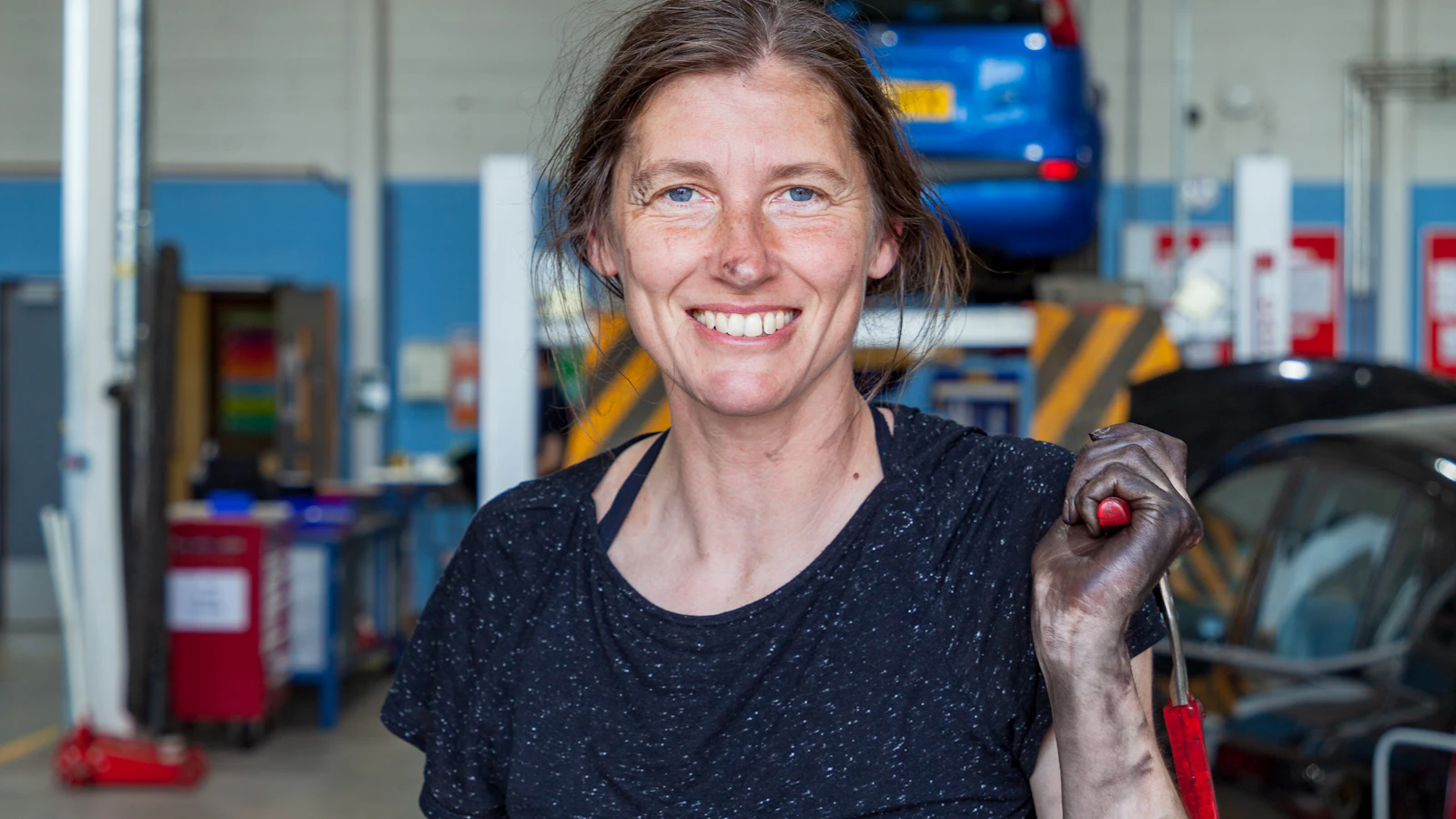 A person holding a wrench inside an automotive workshop.