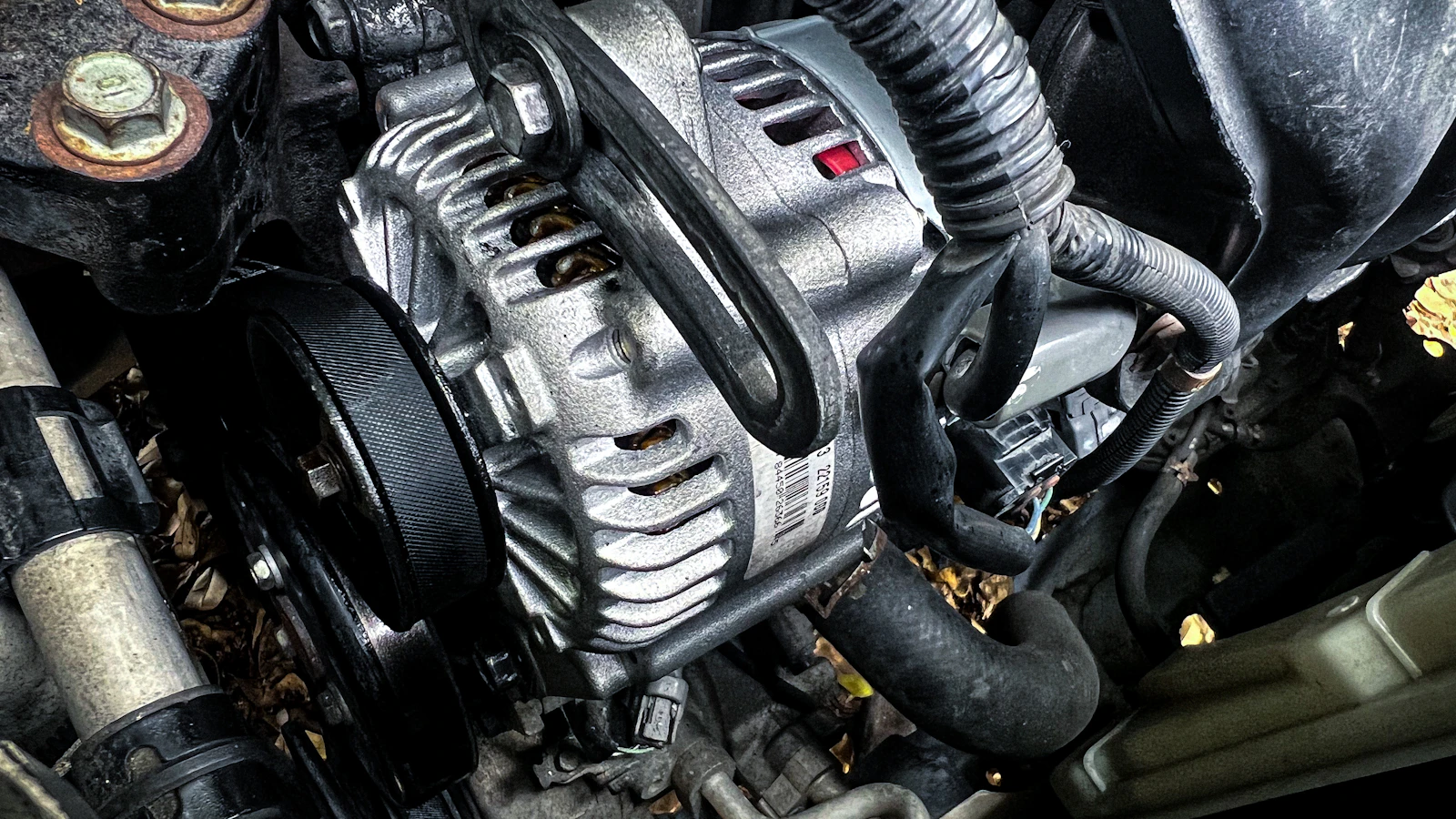 An alternator, hoses and other components inside a vehicle engine compartment.