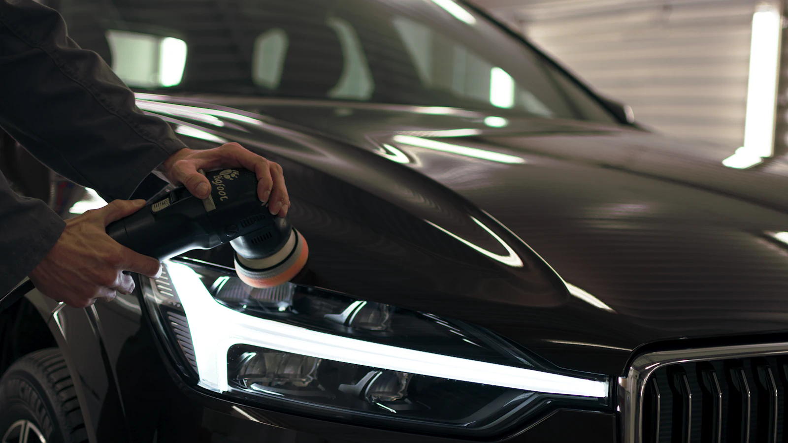 A person using a handheld polisher on the hood of a dark vehicle.