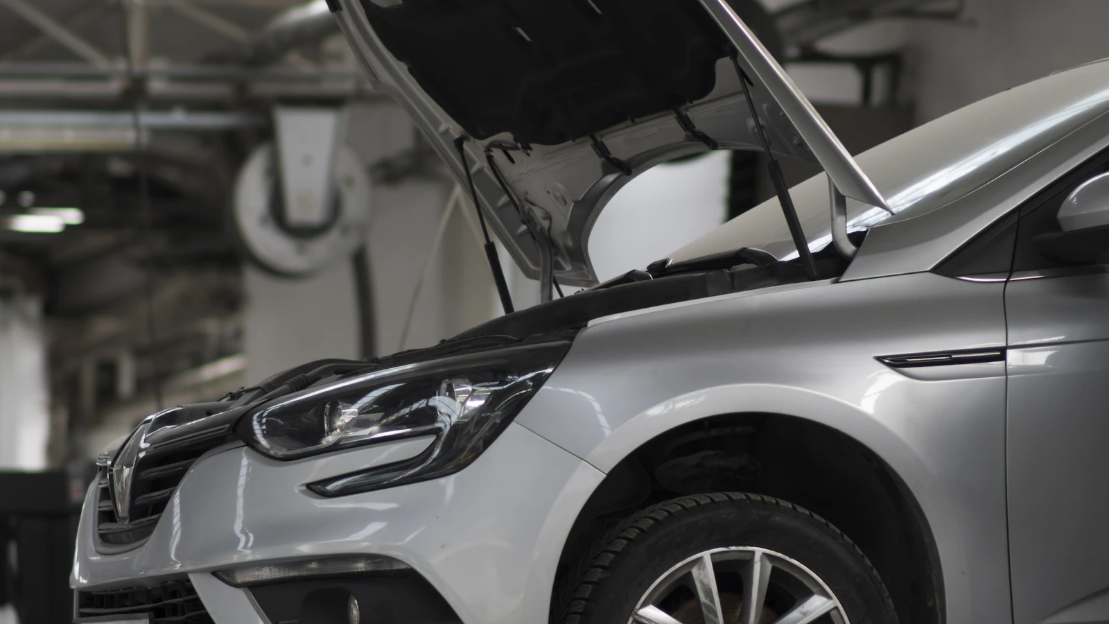 A silver vehicle with its hood open inside a workshop.