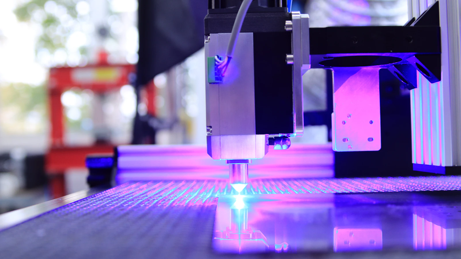 An industrial machine above a work area illuminated with purple light.