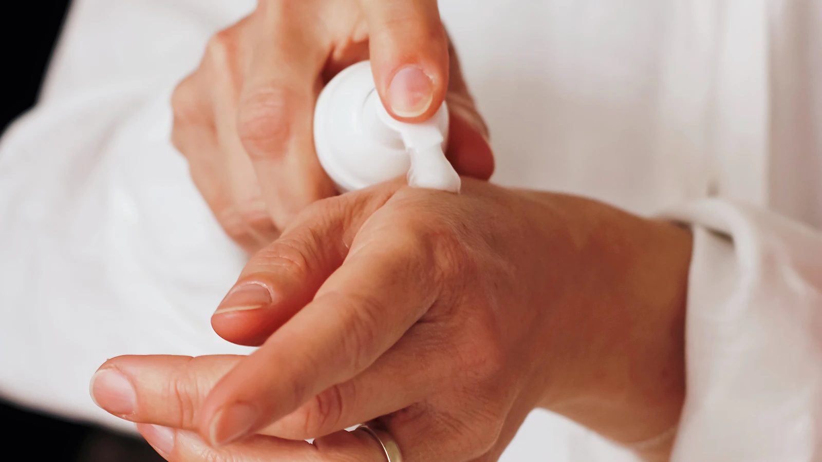 Hands dispensing lotion from a white pump bottle.