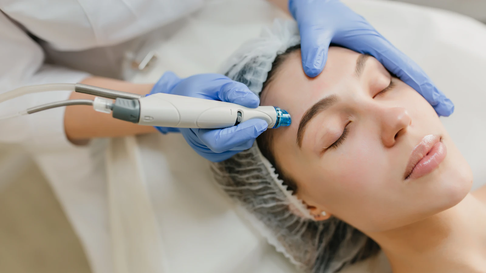 Gloved hands holding a skincare device beside a person’s forehead.