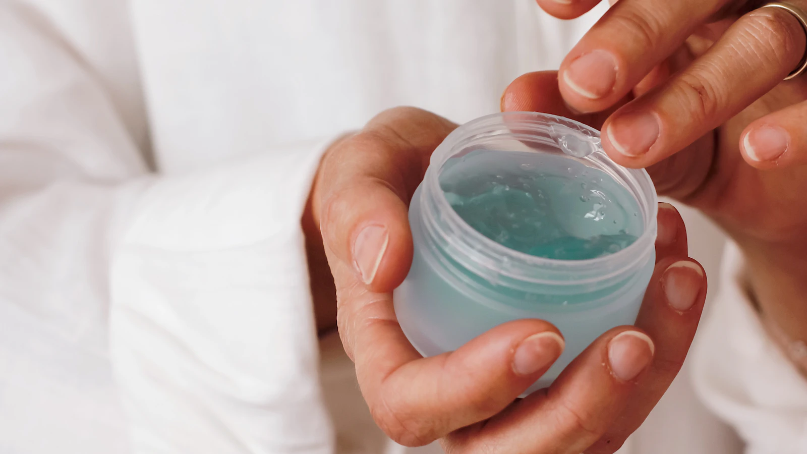 Hands holding an open container of blue skincare gel.