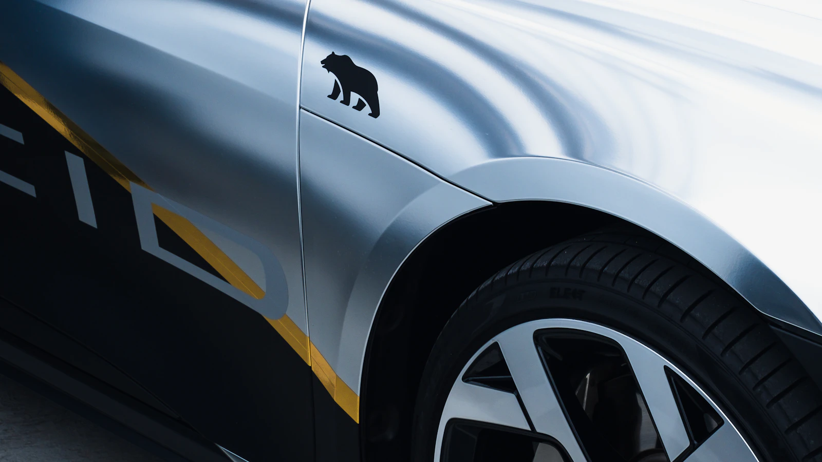 The side of a silver vehicle with black and yellow graphic details.