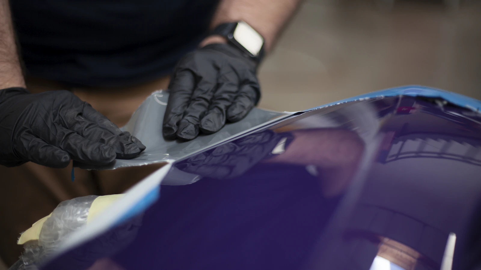 Gloved hands trimming material beside a purple vehicle panel.