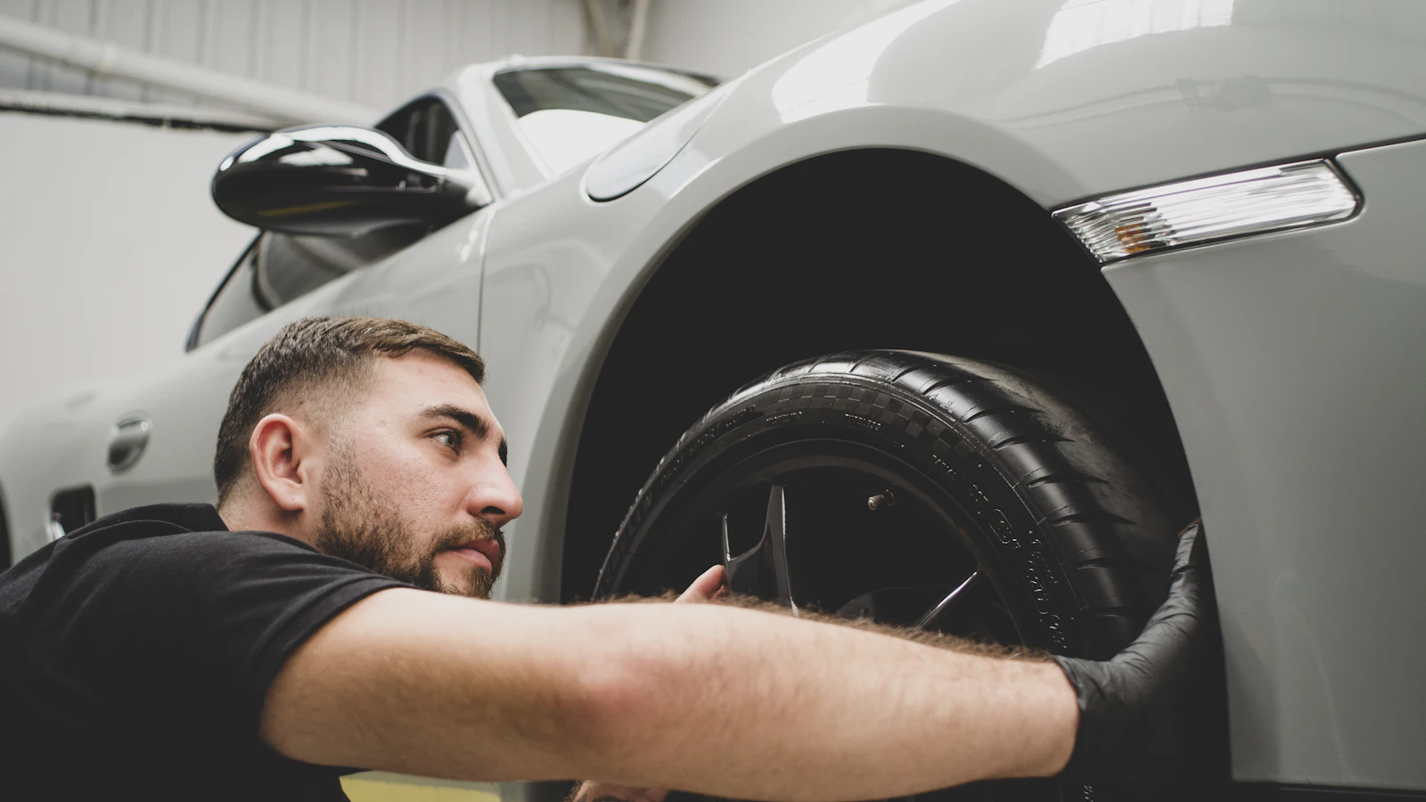 A person working with film beside the front wheel arch of a silver vehicle.