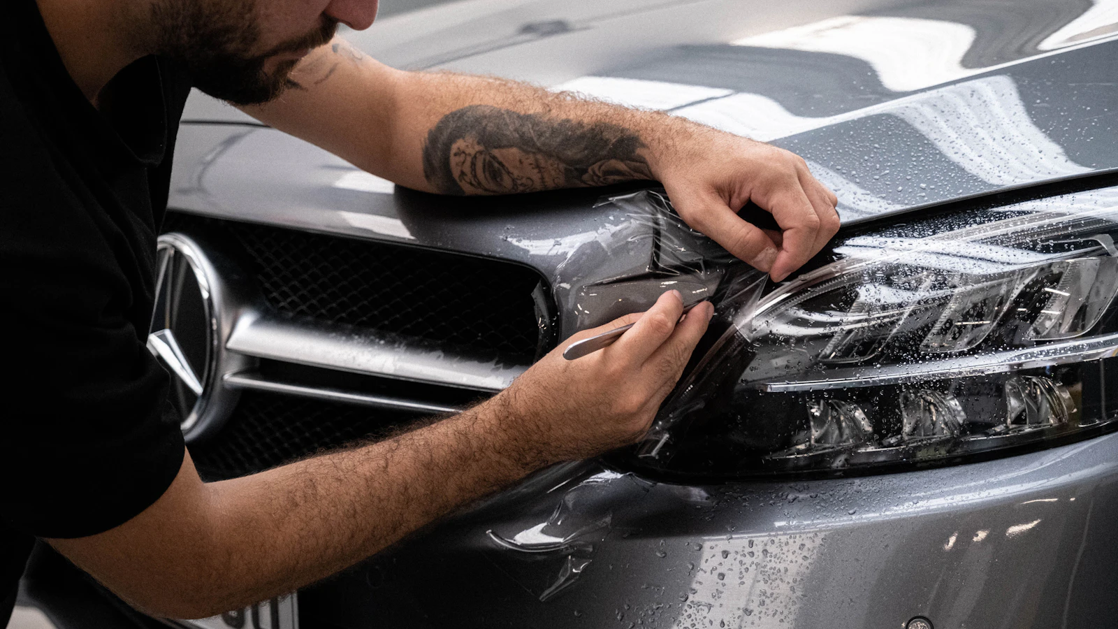 A person applying transparent film around a vehicle headlight.