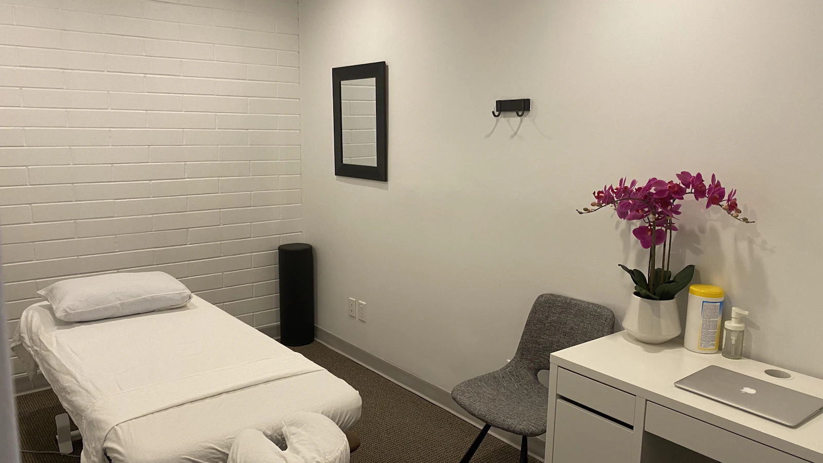 A treatment table beside flowers and a cabinet in a white room.
