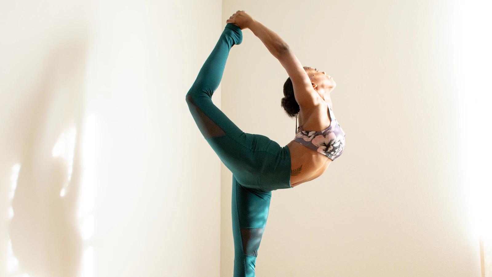 A person balancing in a standing yoga stretch inside a bright room.
