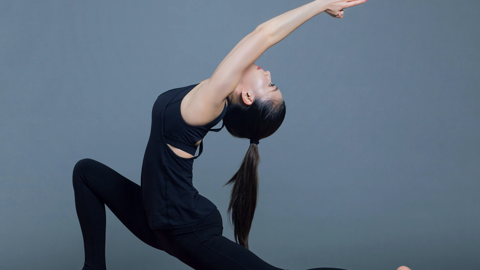 A person stretching in dark exercise clothing against a gray background.