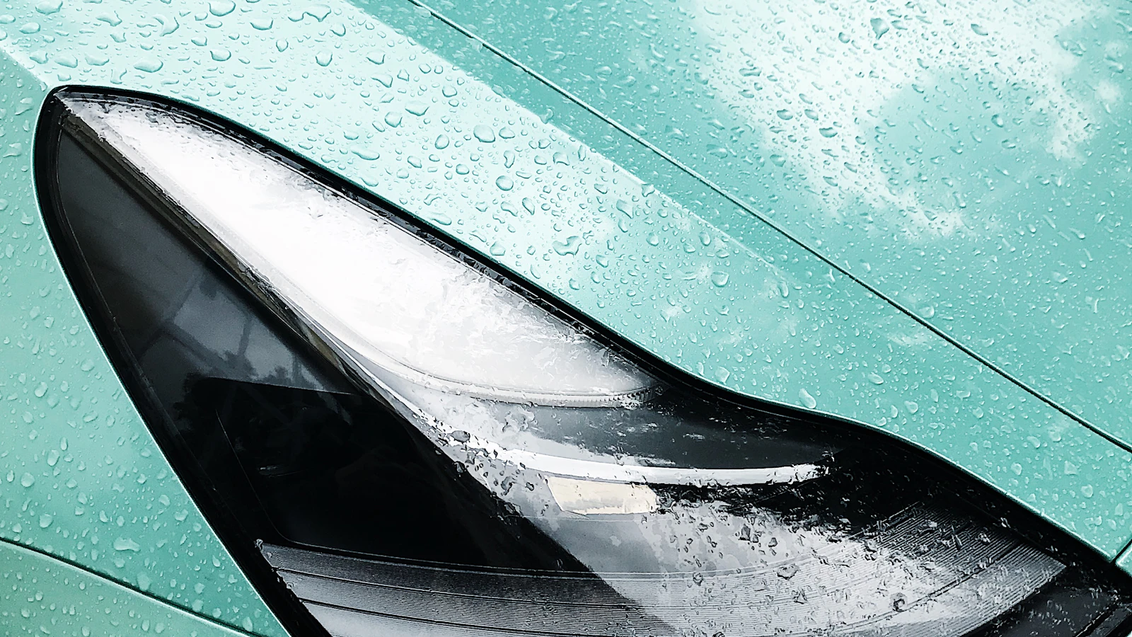 A close view of a wet blue vehicle panel and headlight.