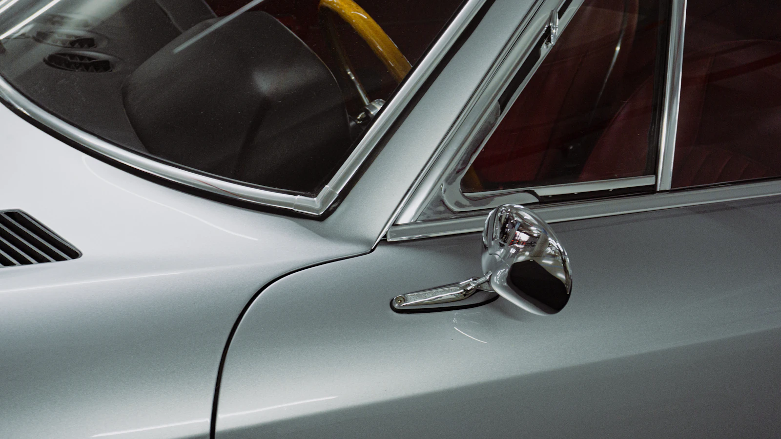 The side window and chrome mirror of a silver classic vehicle.