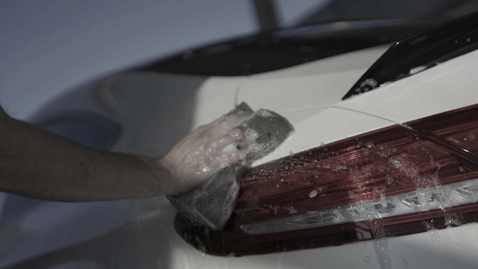 A gloved hand working with transparent film beside a vehicle taillight.