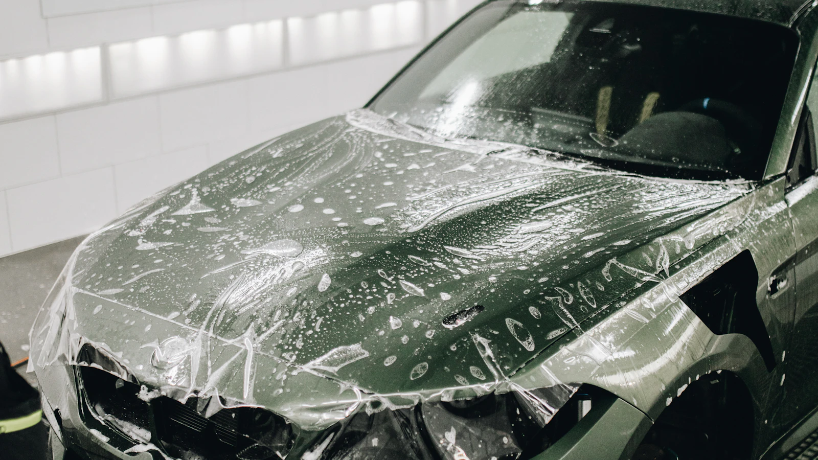 A vehicle hood and front panels covered with wet transparent film inside a workshop.