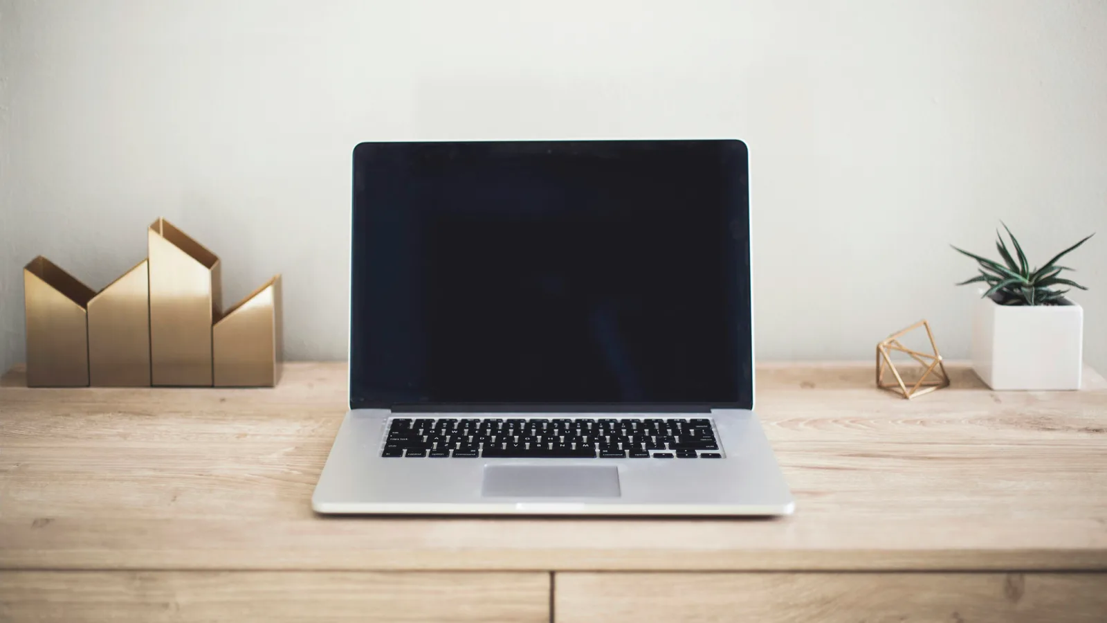Open laptop and geometric desk accessories on a wooden table.