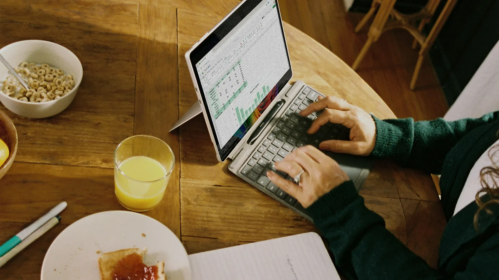 Person working on laptop at wooden table with breakfast.