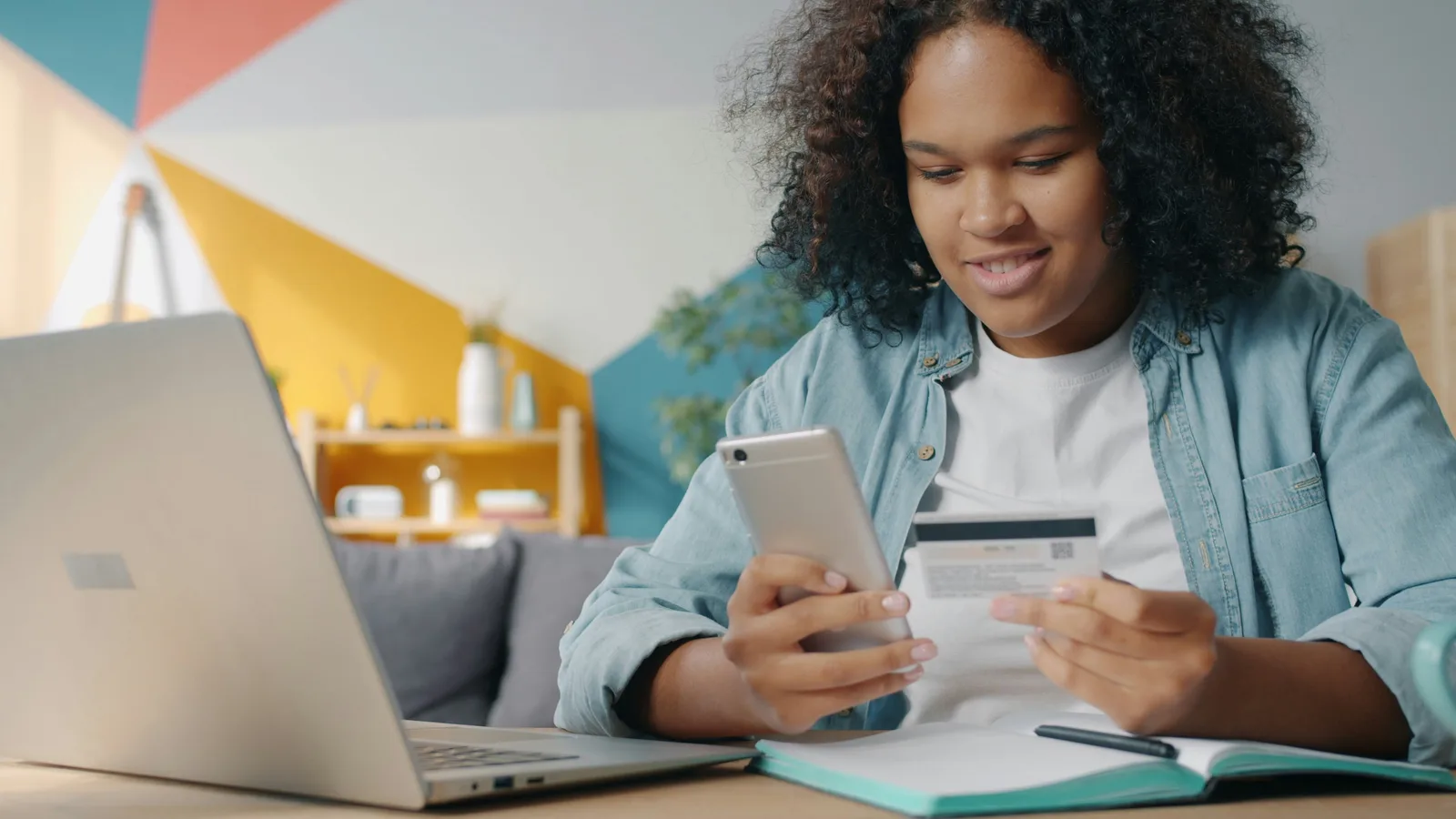 Person checking a payment card beside a smartphone and laptop.