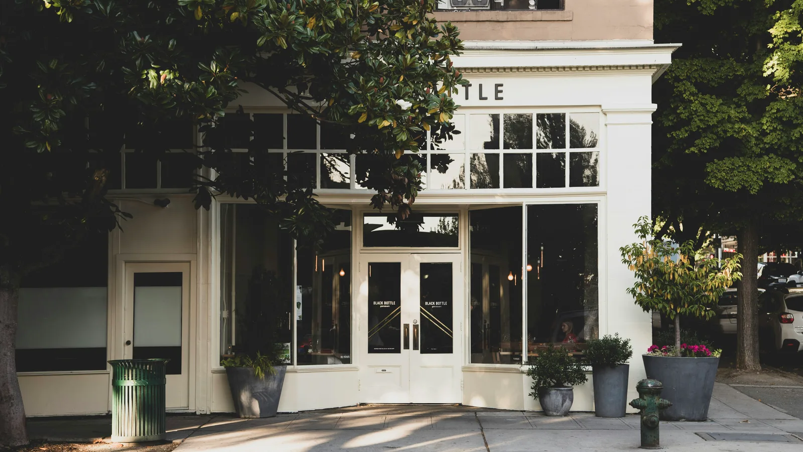 White storefront with tall glass doors and potted plants.