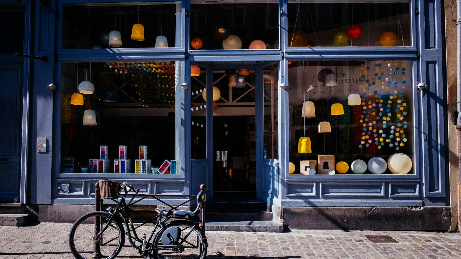 A bicycle parked on a cobblestone sidewalk in front of a lamp shop.
