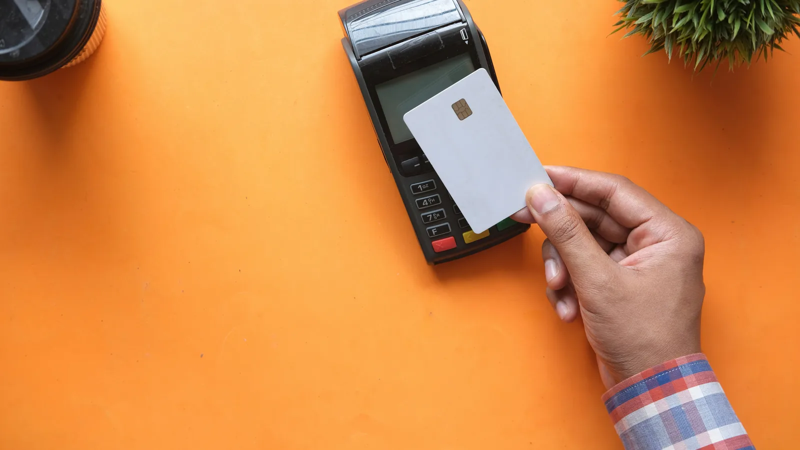 A person holding a blank payment card near a payment terminal on orange.