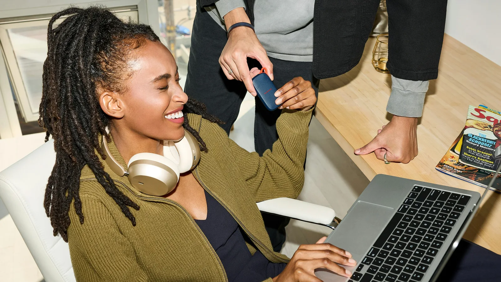 Woman using a laptop while another person hands her a payment card.