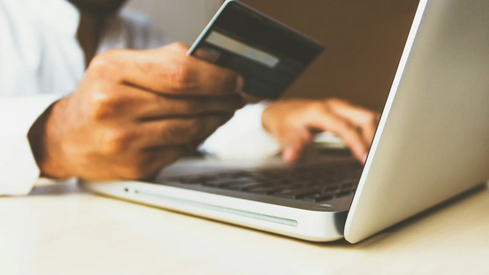 Person holding a payment card while typing on a laptop.