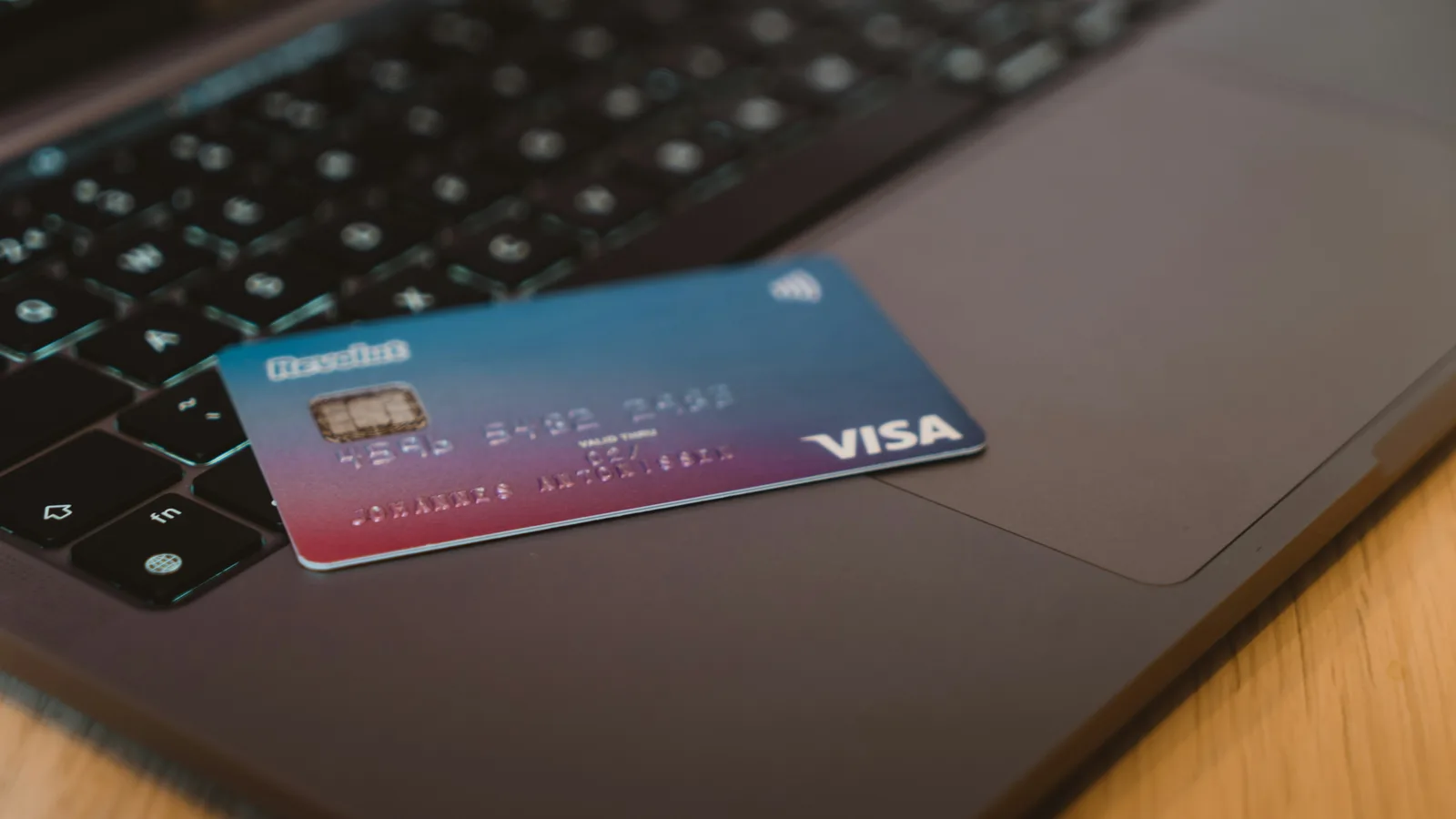 A blue and red gradient debit card resting on a dark laptop keyboard.