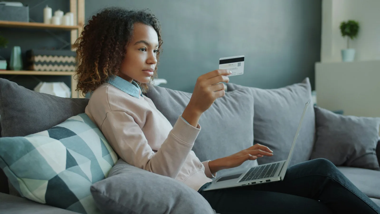 Woman using laptop and payment card on sofa.