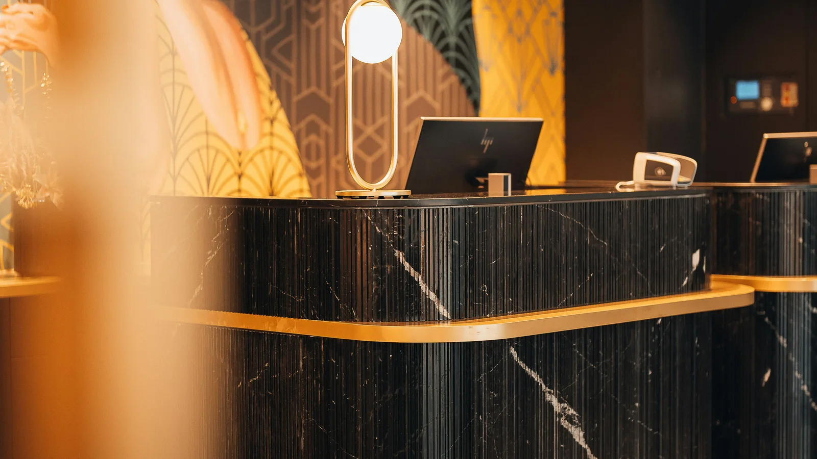 A black marble reception desk with gold trim in a hotel lobby.