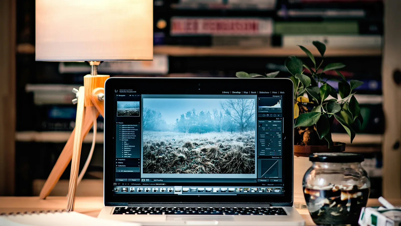 Laptop displaying photo-editing software beside a lamp and stacked books.