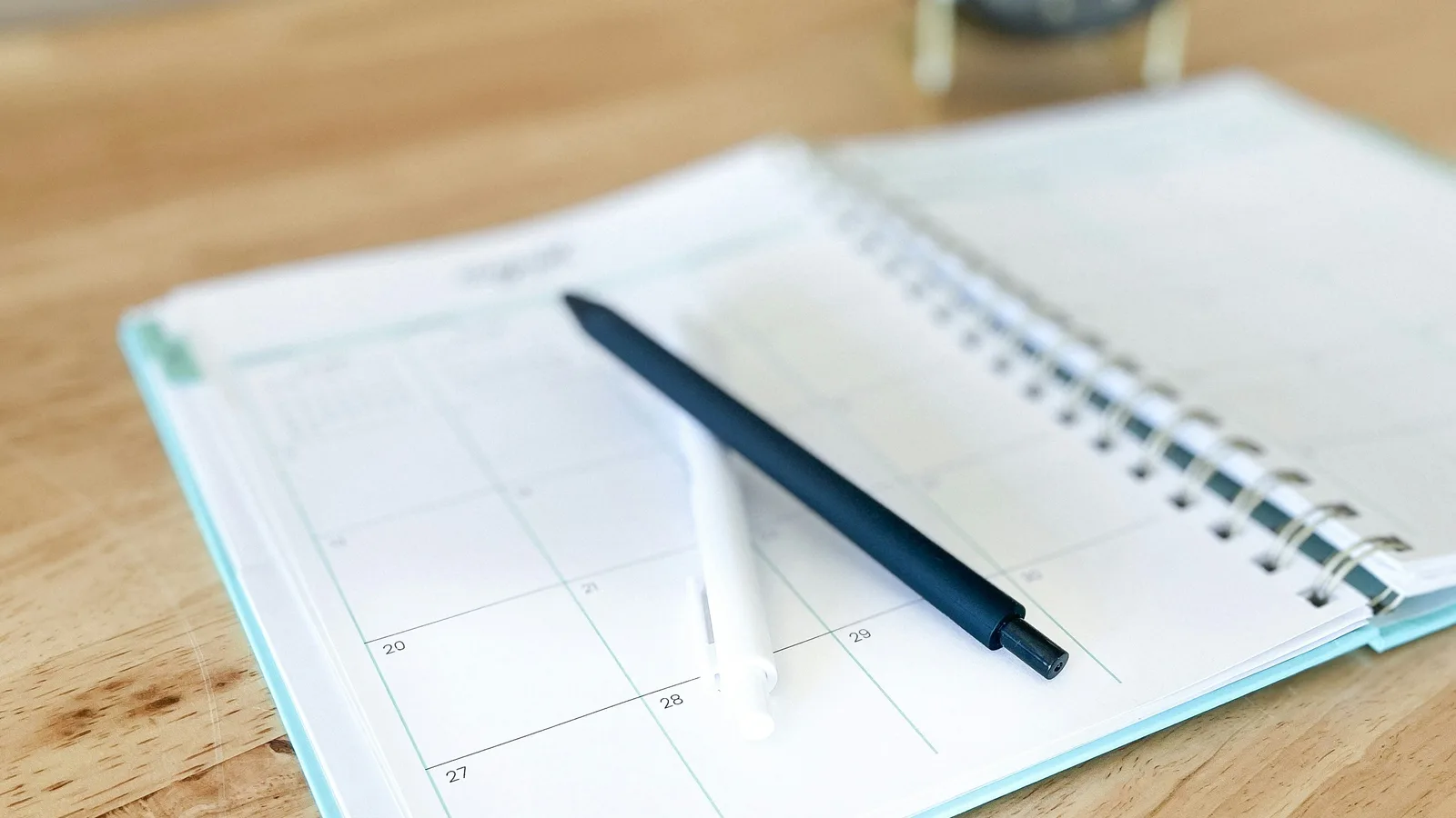 An open planner with a pen on a wooden desk.