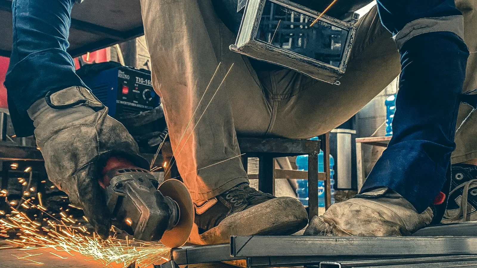 Metalworker using an angle grinder while wearing gloves and a face shield.