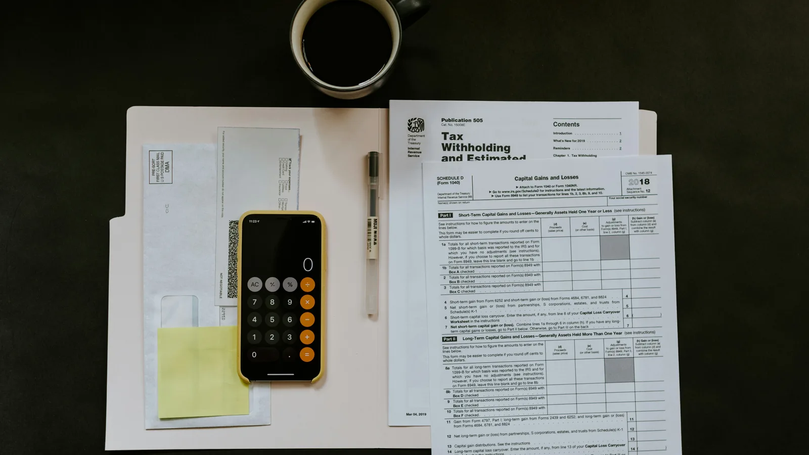 Smartphone calculator beside a tax form, pen and coffee cup.