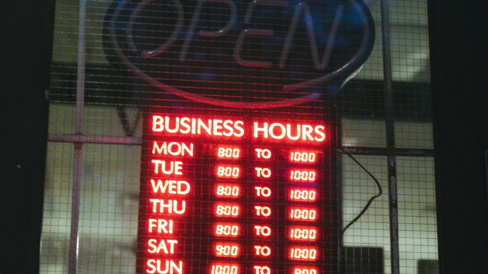 Illuminated business-hours sign below an open sign.