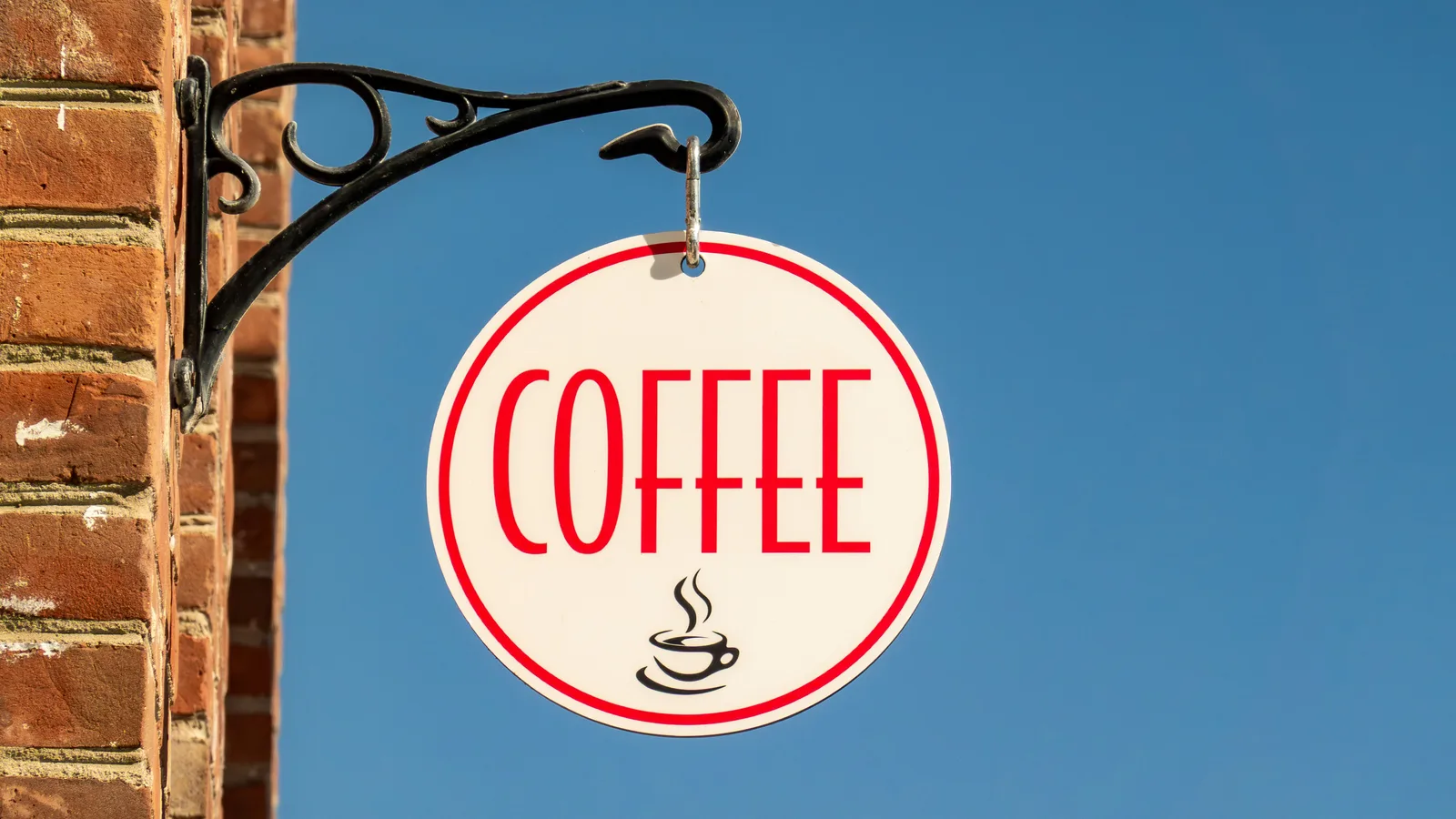 A round coffee sign hangs on a brick wall.