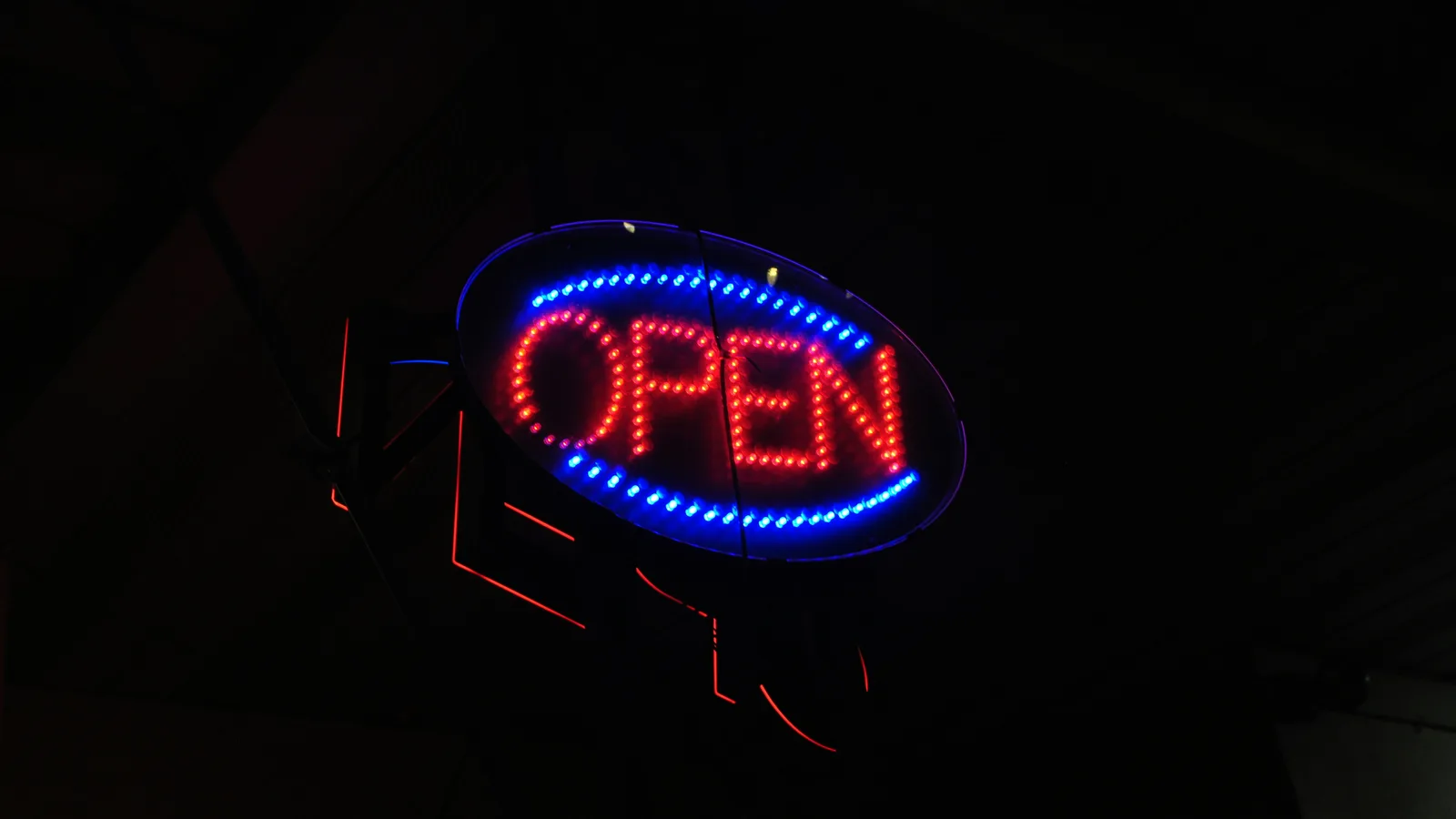 A glowing oval neon sign reading "OPEN" in red and blue against darkness.