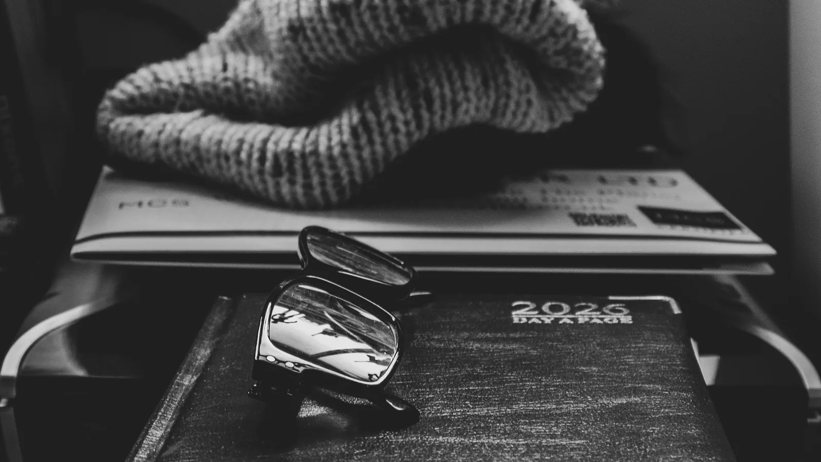 Glasses and a knitted hat beside a closed planner.